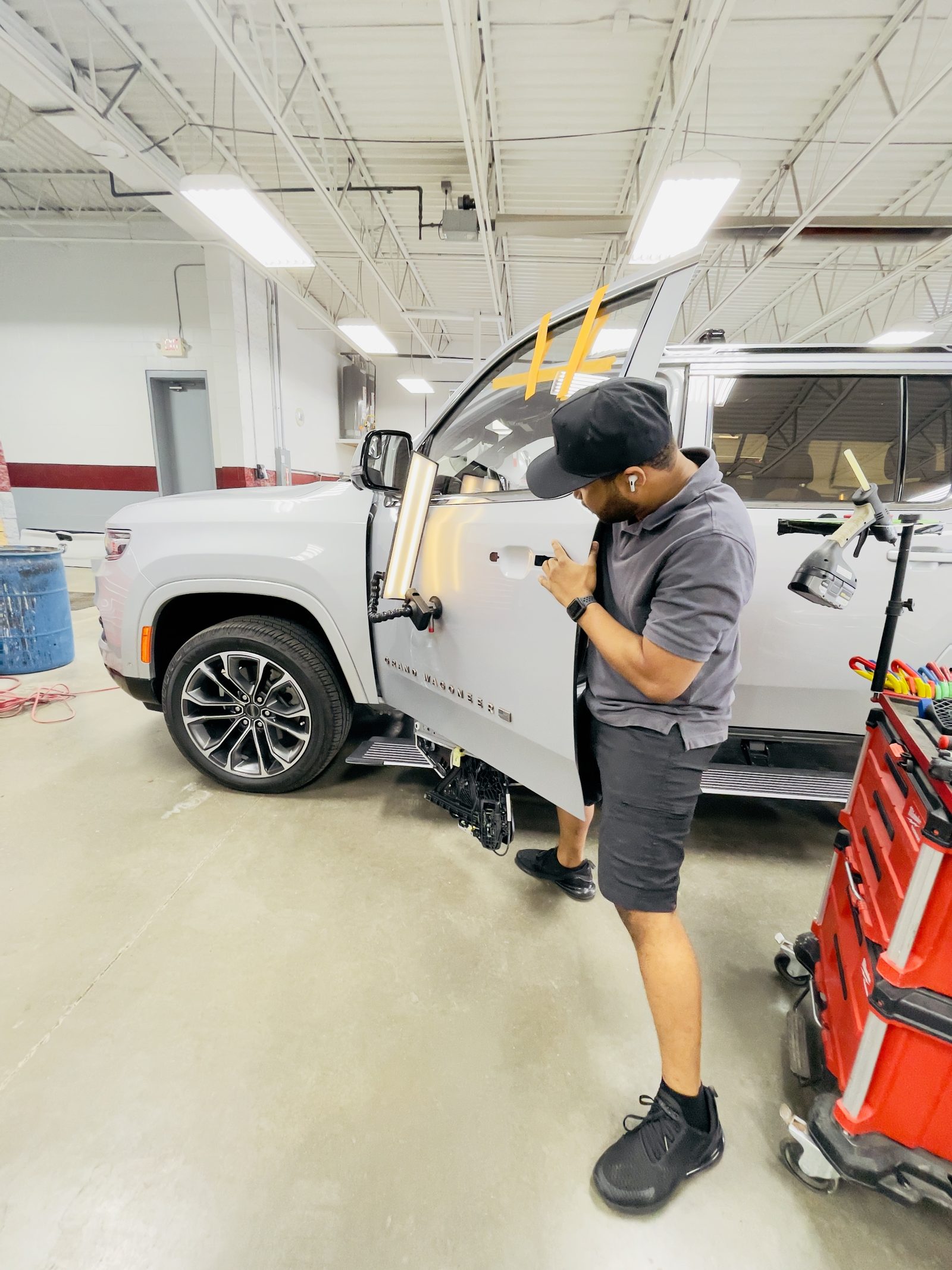 A technician using paintless dent repair tools on a silver SUV door inside the Dent Raptor Auto shop